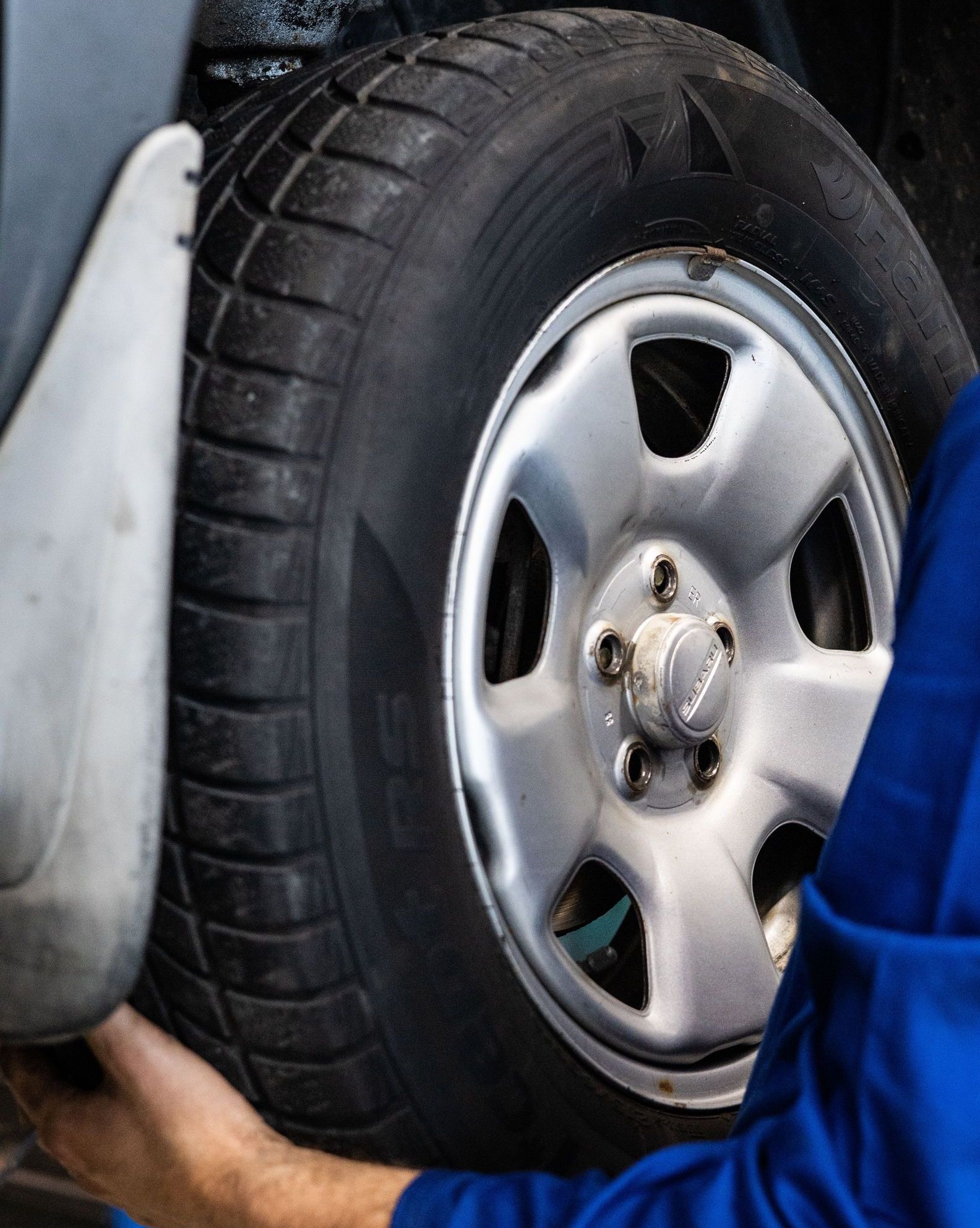 A mechanic in blue uniform closely examines a car wheel for repairs.