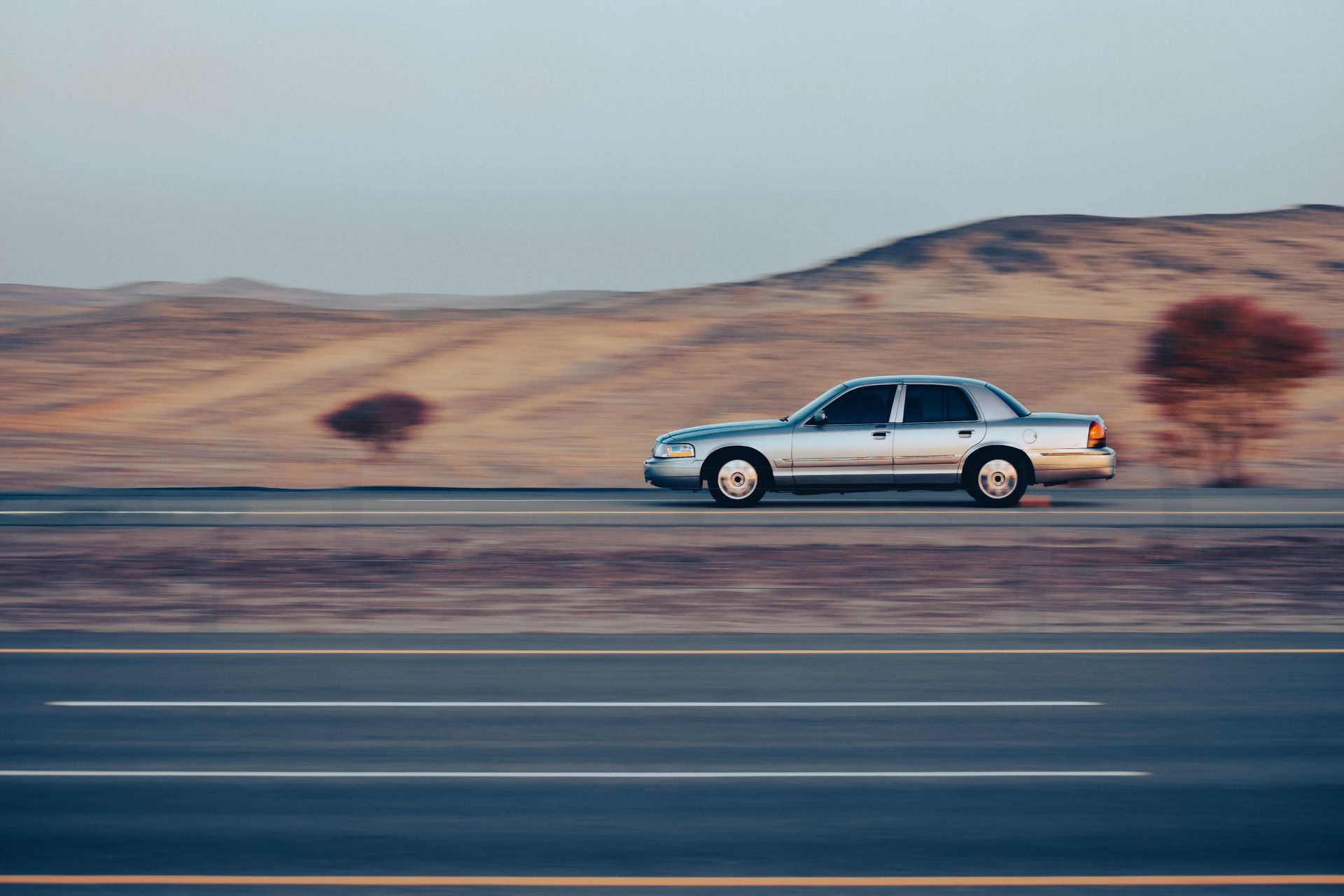A silver car speeds along a highway in a desert setting with blurred motion.